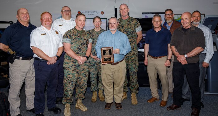 Jason Connerley, the dispatch supervisor of the Quantico Emergency Communication Center, middle, poses for a group photo with attendees during his award ceremony at the ECC on Marine Corps Base Quantico, Virginia, April 27, 2026. The Public Safety Communications Center Supervisor of the Year Award is given for professional achievement and dedication, something that Connerley demonstrated throughout his time as an important asset of MCB Quantico and the ECC. (U.S. Marine Corps photo by Lance Cpl. Lynsee Avila-Ramirez)