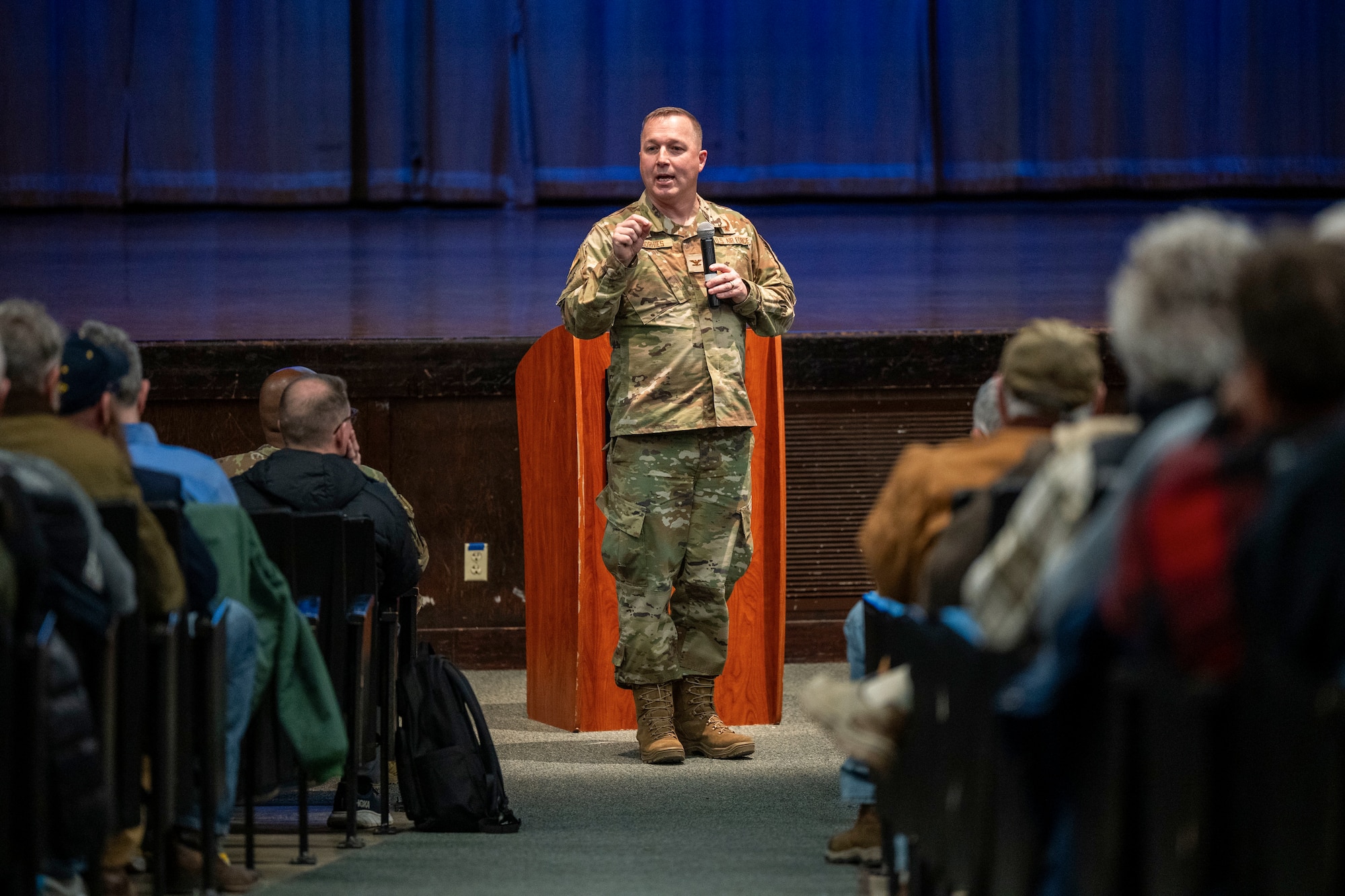 A man in uniform speaking at the front of a theater.