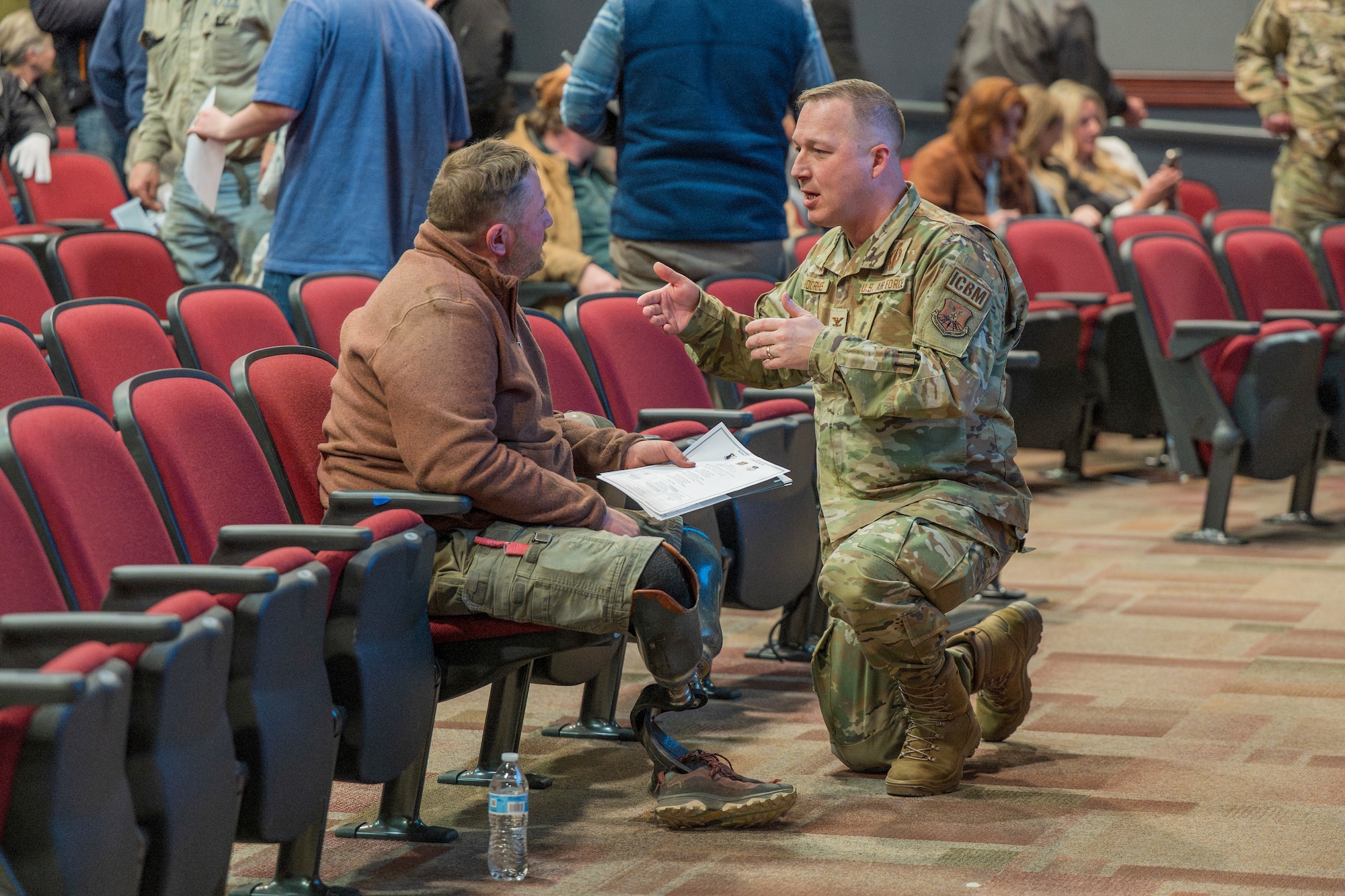 A man in military uniform kneeling speaking to a man sitting.
