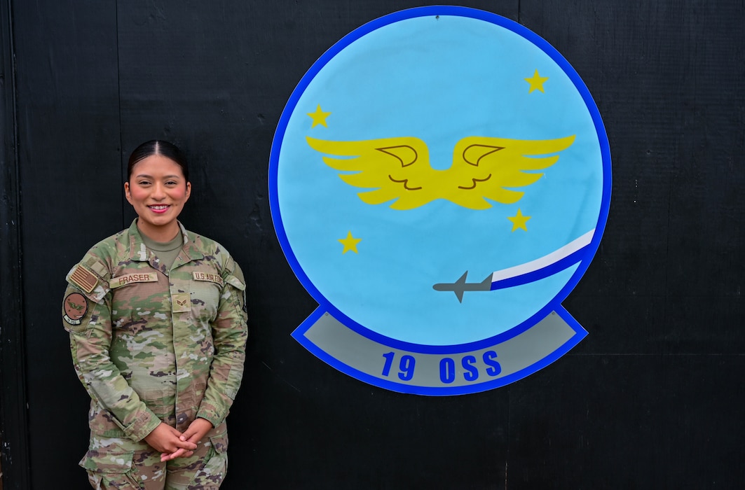 A woman stands smiling beside a "19 oss" logo.