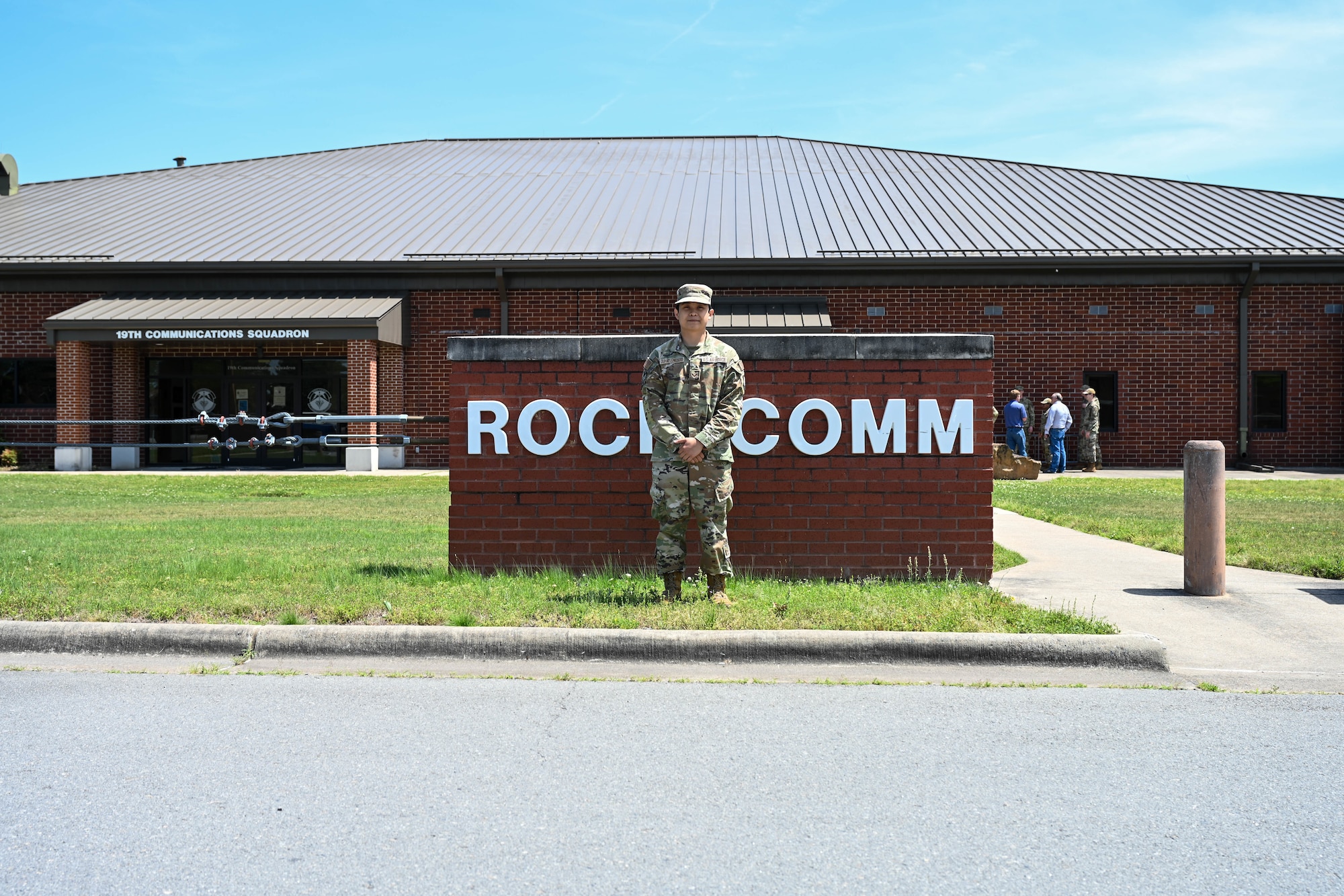 A man is posing for a picture in front of a "Rock Comm" sign.