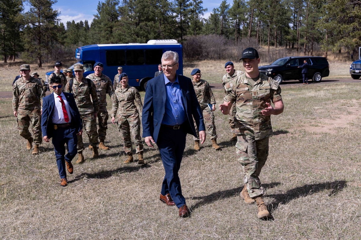 A group of Cadets and men in suits walk away from a bus.