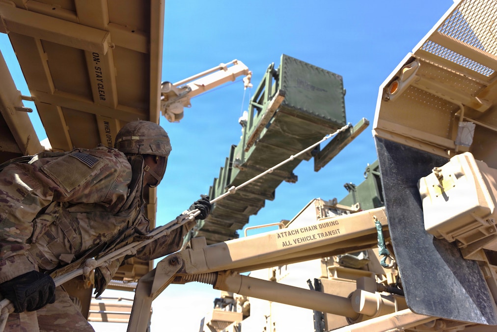 A soldier reaches up using a long pole to reload a missile launcher.