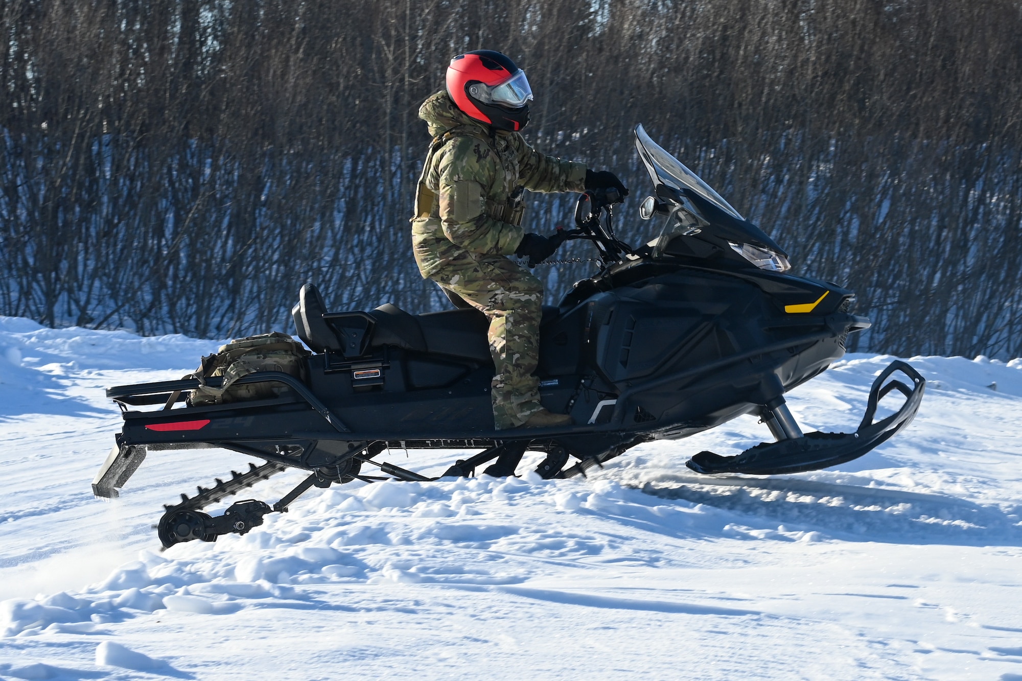 Airman 1st Class Ryan Smith, a 673d Security Forces Squadron defender, drives a snowmachine over a short hill during the Arctic Combat Development Course on Joint Base Elmendorf-Richardson, March. 26, 2026. Comfortably operating a snowmachine in an austere environment is a major portion of the ACDC and requires no prior experience to attend the course. (U.S. Air Force photo by Airman 1st Class Eli A. Rose)