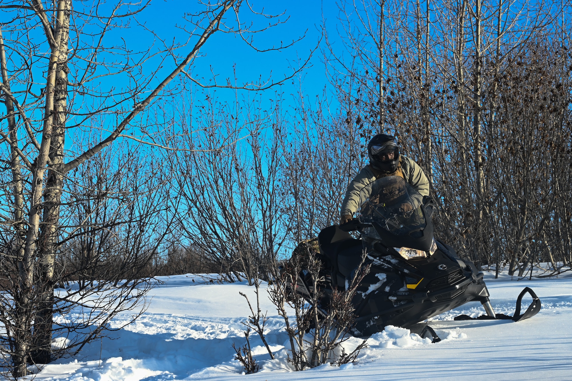 U.S. Air Force Staff. Sgt. Cameron Christopher, a 673d Security Forces Squadron defender, drives a snowmachine during the Arctic Combat Development Course on Joint Base Elmendorf-Richardson, March 26 2026. Snowmachine competency is a cornerstone of ACDC, which seeks to better equip servicemembers for combat scenarios in austere arctic scenarios, further enhancing homeland defense. (U.S. Air Force photo by Airman 1st Class Eli A. Rose)