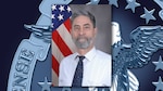 Graphic featuring an official photo of a man with a gray beard, wearing a buttoned shirt and tie