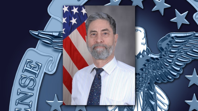 Graphic featuring an official photo of a man with a gray beard, wearing a buttoned shirt and tie