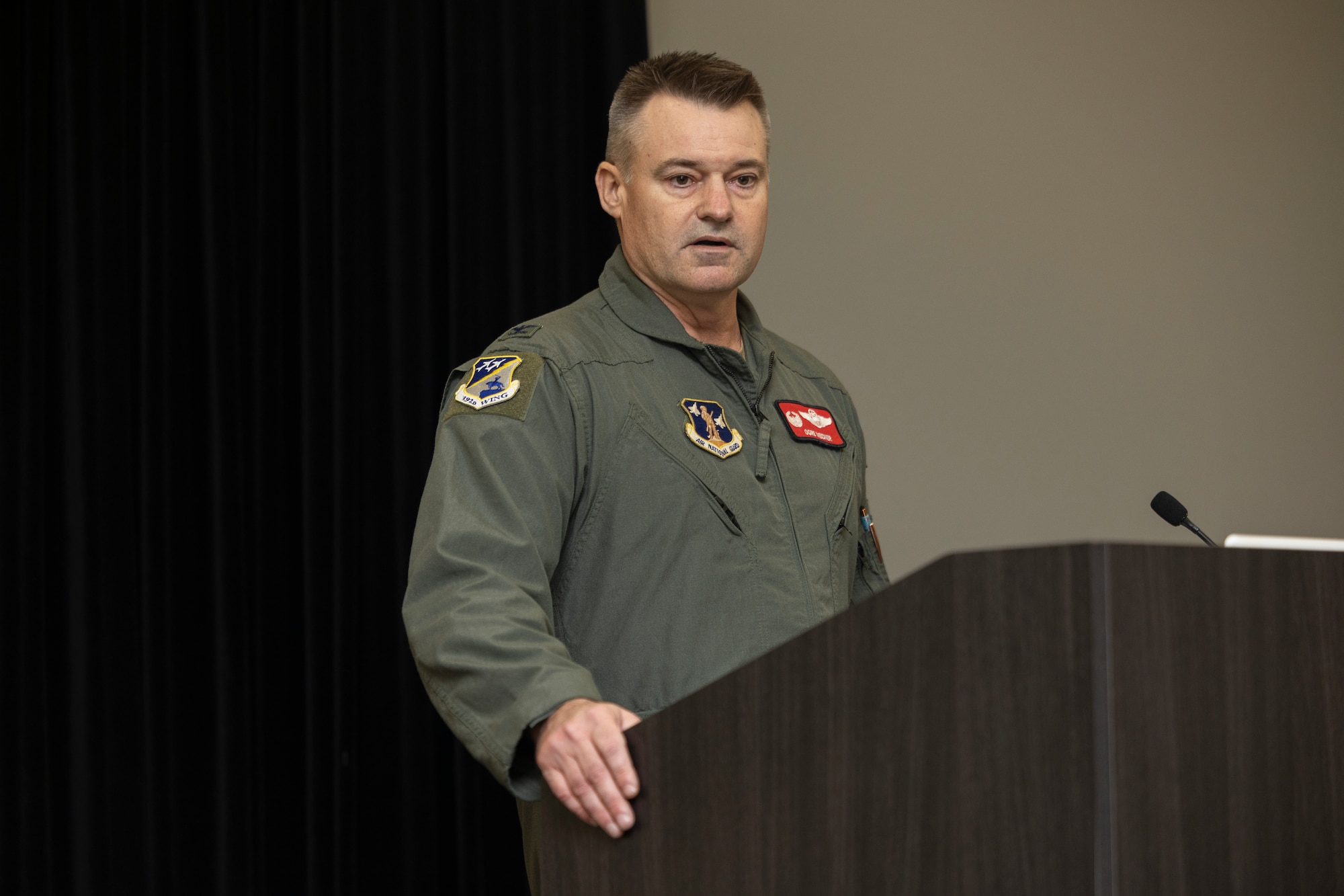 Col. Andrew M. Weidner is standing behind a podium, speaking.