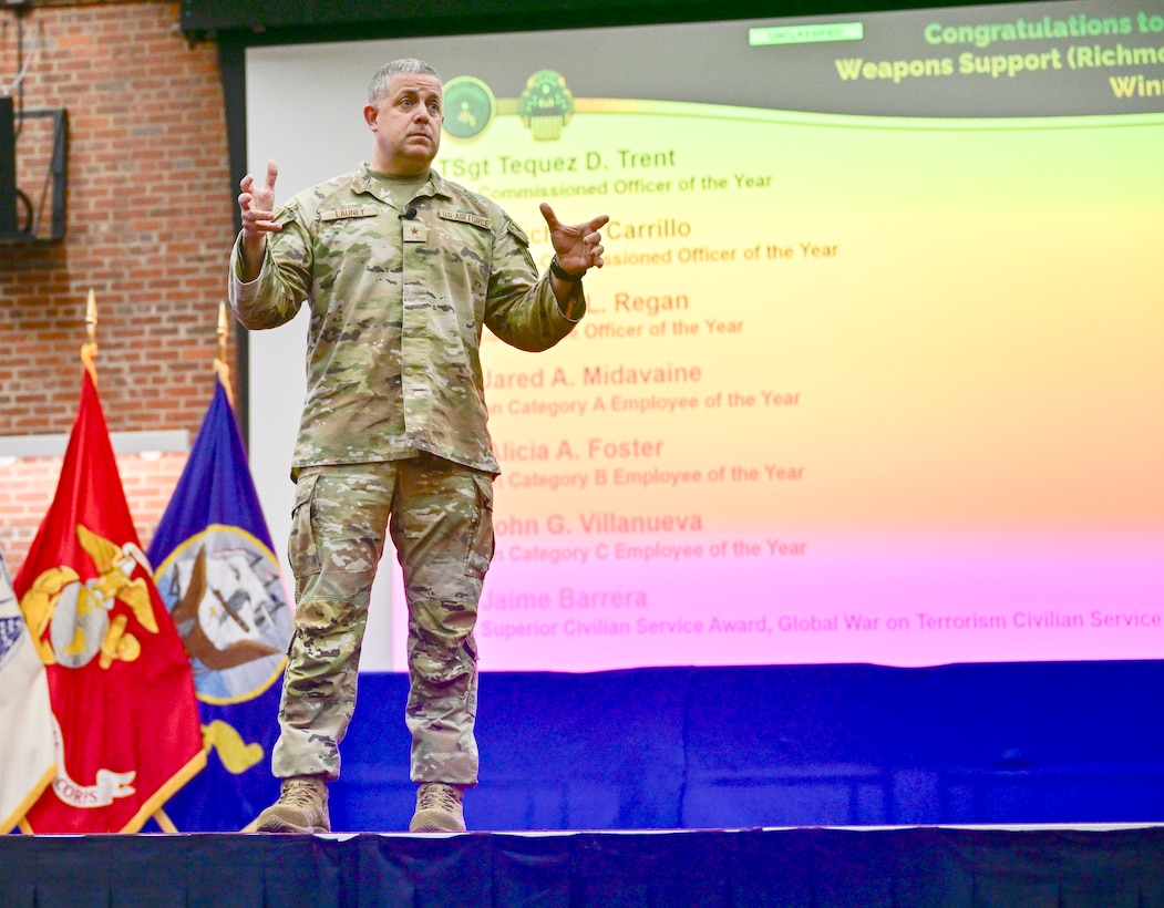 A uniformed man stands on a stage speaking to an audience