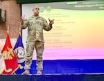 A uniformed man stands on a stage speaking to an audience