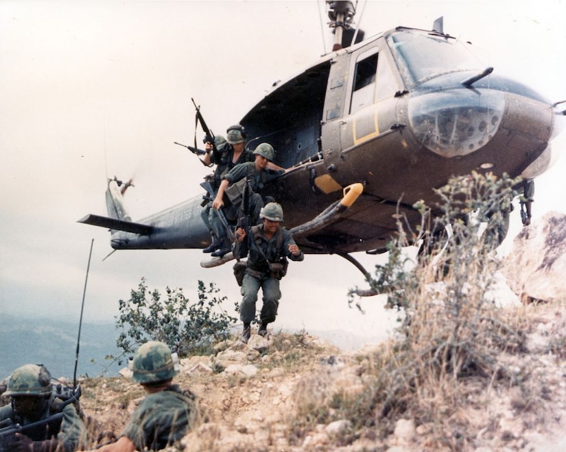 Soldiers jump from a helicopter atop a hill.