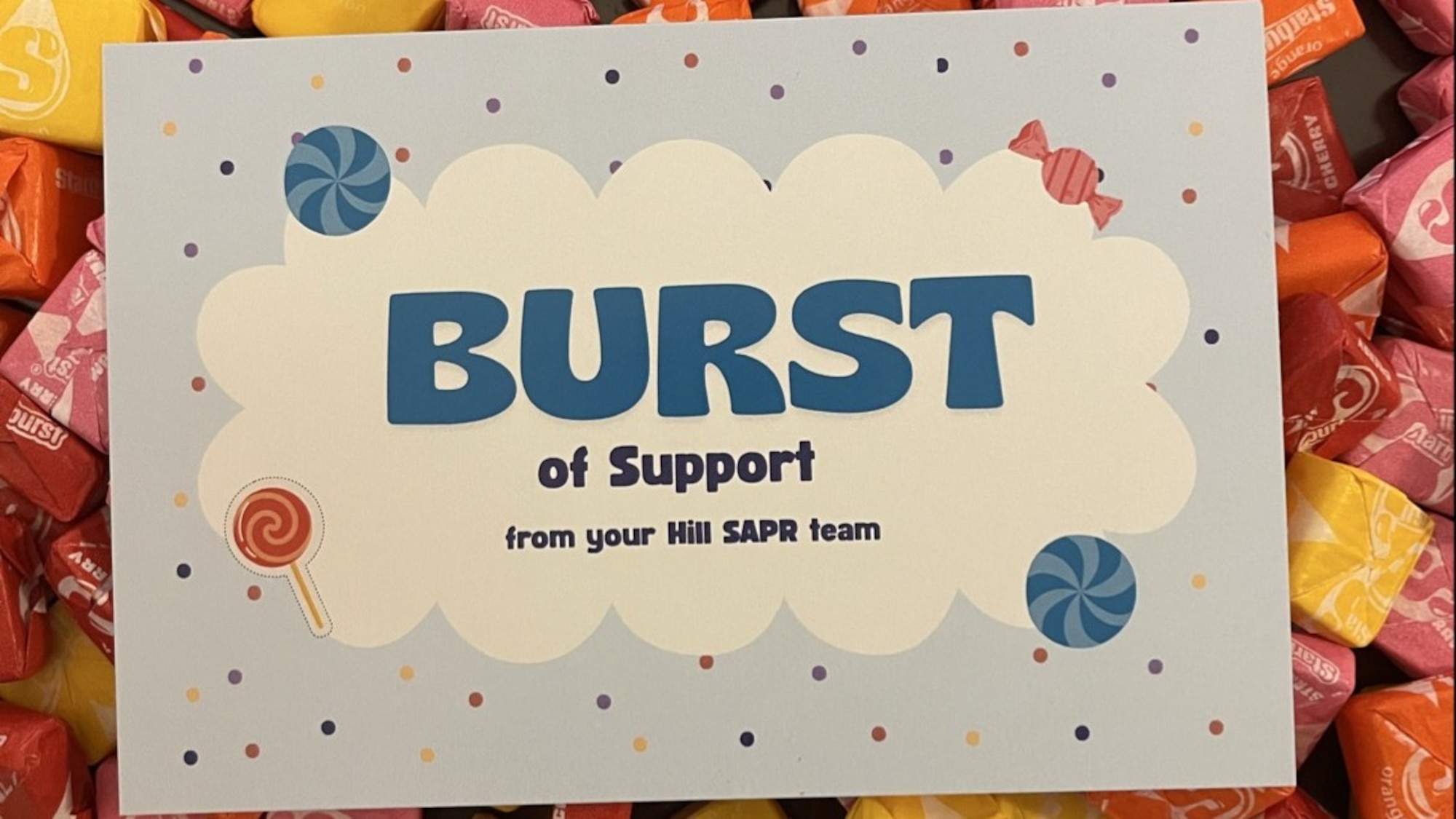 An overhead view of colorful Starburst candies with a promotional card for the Hill AFB SAPR office laid on top.