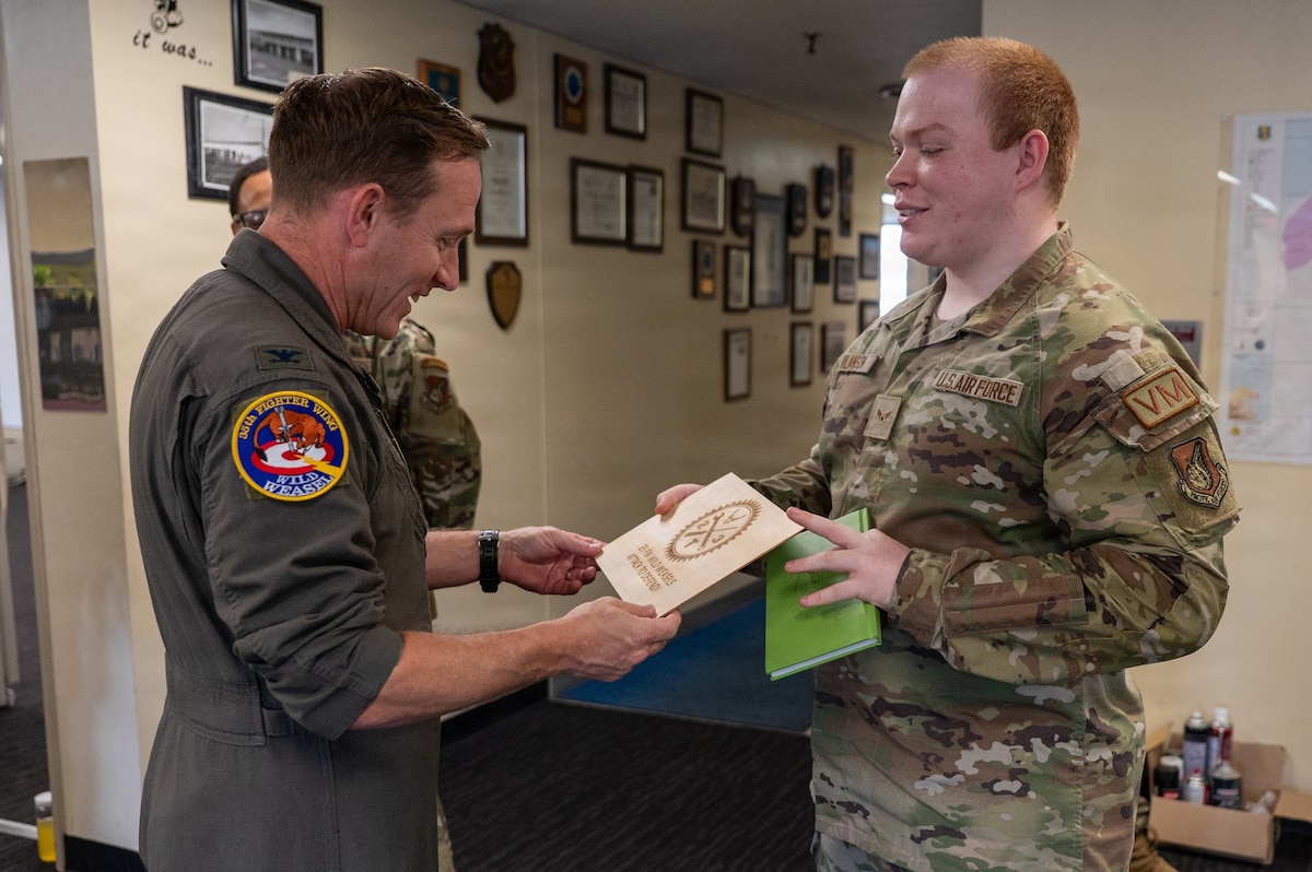 U.S. Air Force Airman 1st Class Zachary Wilkinson, right, 35th Logistics Readiness Squadron fleet management and analysis technician, presents a custom-printed item to Col. Paul Davidson, 35th Fighter Wing (FW) commander, at Misawa Air Base, Japan, April 27, 2026. Davidson selected Wilkinson  as Wild Weasel of the Week for his professionalism and dedication to supporting installation needs and enhancing 35th FW readiness. (U.S. Air Force photo by Airman 1st Class Angelica Winther)
