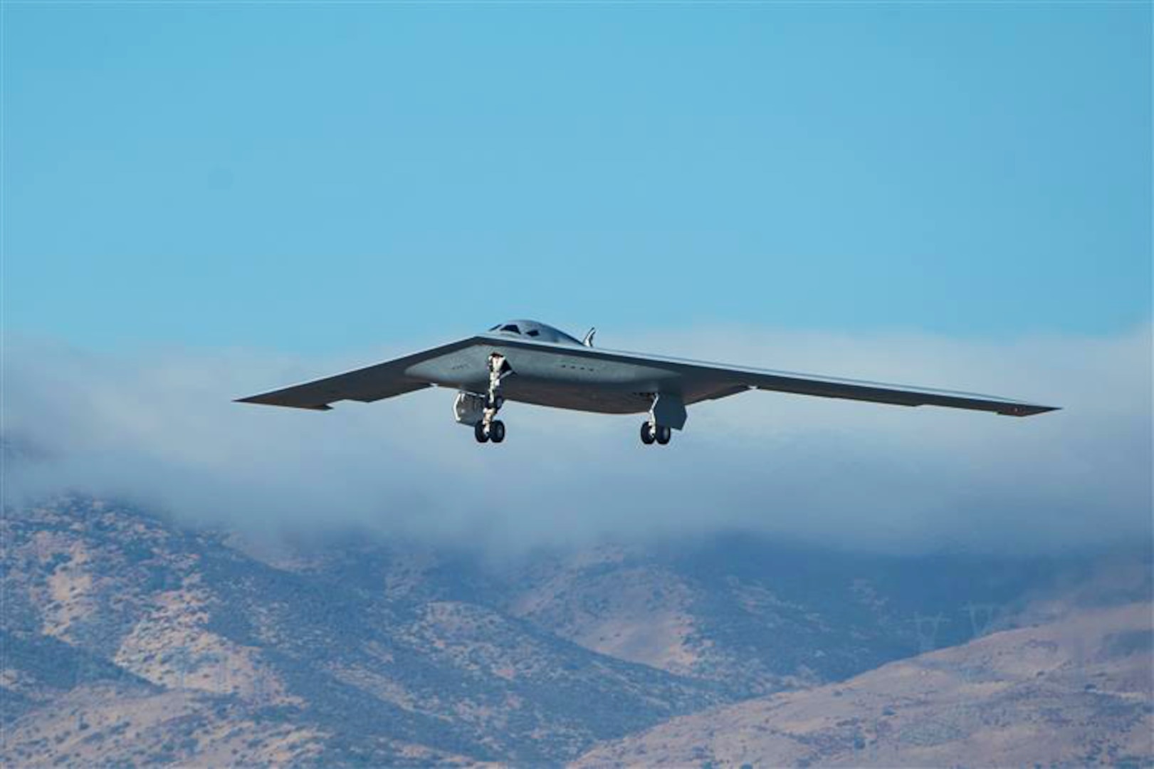A military bomber aircraft flies above mountains.