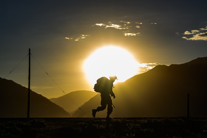 A silhouette of an Airman rucking with the sun just above the mountains.