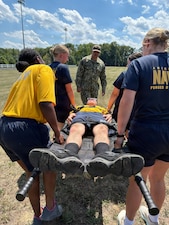 U.S. Navy Hospital Corpsman 1st Class Antonio Armenteros, center background, mentors medical personnel as they execute a tactical litter carry during a Tactical Combat Casualty Care (TCCC) evolution at Naval Support Facility (NSF) Indian Head, Maryland. The joint training scenario—combining personnel from Navy Medical Readiness and Training Unit (NMRTU) Dahlgren, NMRTC-Detachment Indian Head, and NMRTC-Detachment Joint Base Andrews—was held during a special "Warrior Wednesday" block commemorating the 128th Navy Hospital Corpsman Birthday. Under Armenteros' guidance, the drill reinforced patient movement techniques, team coordination, and field transport protocols, honoring the rating's heritage through hands-on operational readiness training