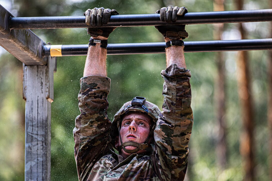 U.S. Army Pfc. Logan Ryan, with 7th Army Training Command, hangs from the overhead traverse obstacle during the U.S. Army Europe and Africa Best Squad Competition at Grafenwoehr Training Area, Germany, July 31, 2026. Teams across U.S. Army Europe and Africa meet at Grafenwoehr Training Area, Germany, to compete for the title of Best Squad, July 30-August 6, 2026. The event tests the squad’s effectiveness, communication, and overall cohesion, as well as the individual Soldier’s technical and tactical proficiency, endurance, and fortitude. This competitive training event exercises a full range of squad-level skills, highlighting professional excellence and knowledge to determine the command’s top teams. Winners of this competition will advance to represent U.S. Army Europe and Africa at the Army Best Squad Competition. (U.S. Army Reserve photo by Sgt. Addison Shinn)