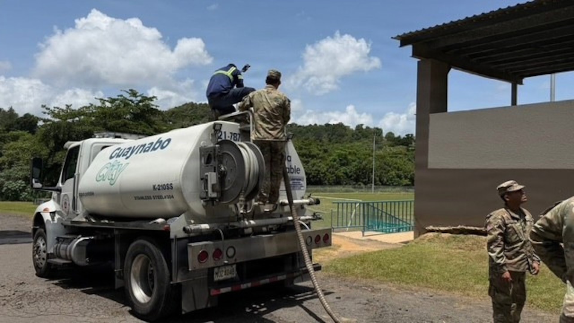 U.S. Army Soldiers work alongside a civilian contractor atop a Guaynabo City municipal water tanker truck (K-210SS) during a water distribution operation at an unidentified facility in Puerto Rico.