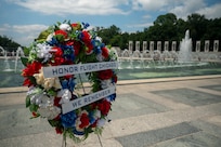 A wreath with red, white and blue flowers saying "Honor Flight Chicago, We remember" is displayed in front of the WWII memorial