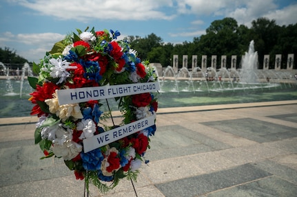 A wreath with red, white and blue flowers saying "Honor Flight Chicago, We remember" is displayed in front of the WWII memorial