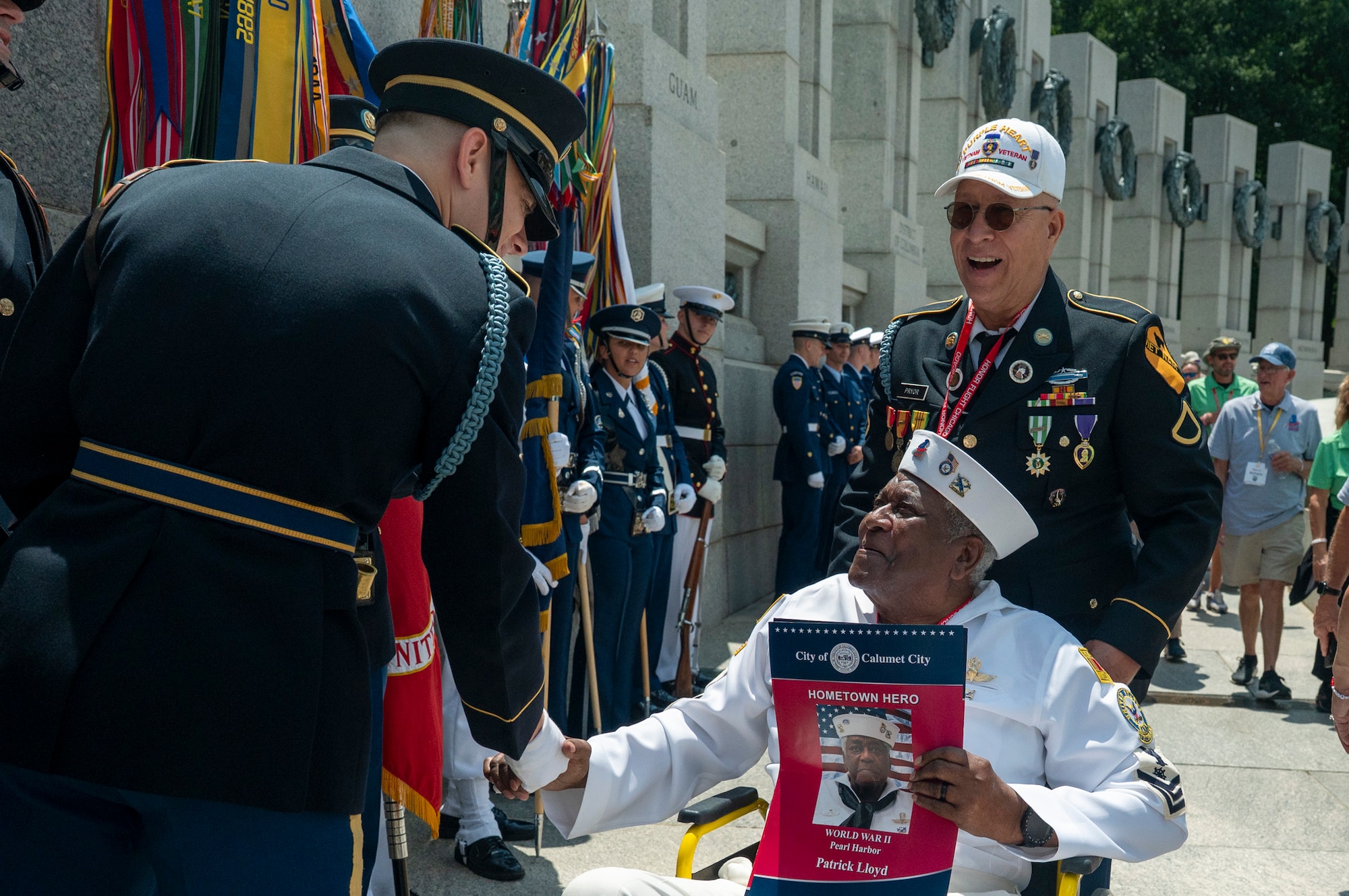 WWII veteran wearing his uniform shakes hands with members of the Joint Armed Forces Color guard in front of the WWII memorial