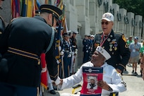 WWII veteran wearing his uniform shakes hands with members of the Joint Armed Forces Color guard in front of the WWII memorial