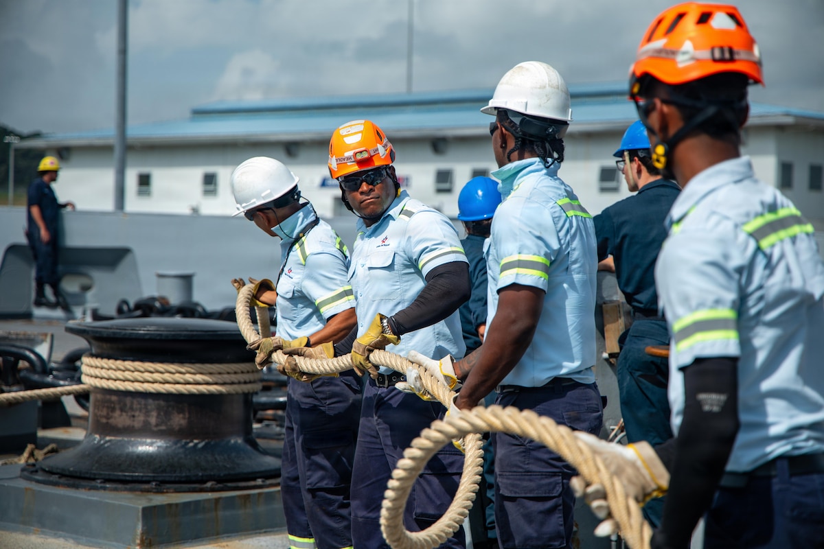 Four men in uniforms and hard hats secure a rope to a dock fitting.