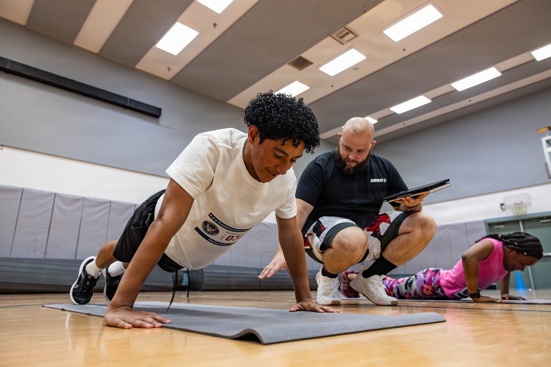 Young athletes do push-ups during the Presidential Fitness Test at Marine Corps Air Ground Combat Center Community Center, Twentynine Palms, California, July 23, 2026. The Presidential Fitness Test is for children ages 6 to 18 and encourages building strength, endurance, and healthy habits while striving for personal improvement. (U.S. Marine Corps photo by Lance Cpl. Cody Fitzgerald)