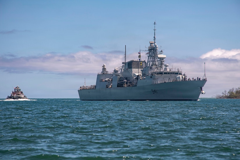 A large ship sails through water with a smaller boat behind it.
