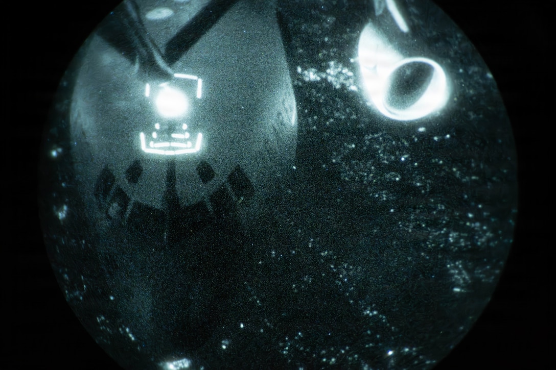 A close-up of an aircraft extending its boom to another aircraft in the dark with white specks throughout the background.