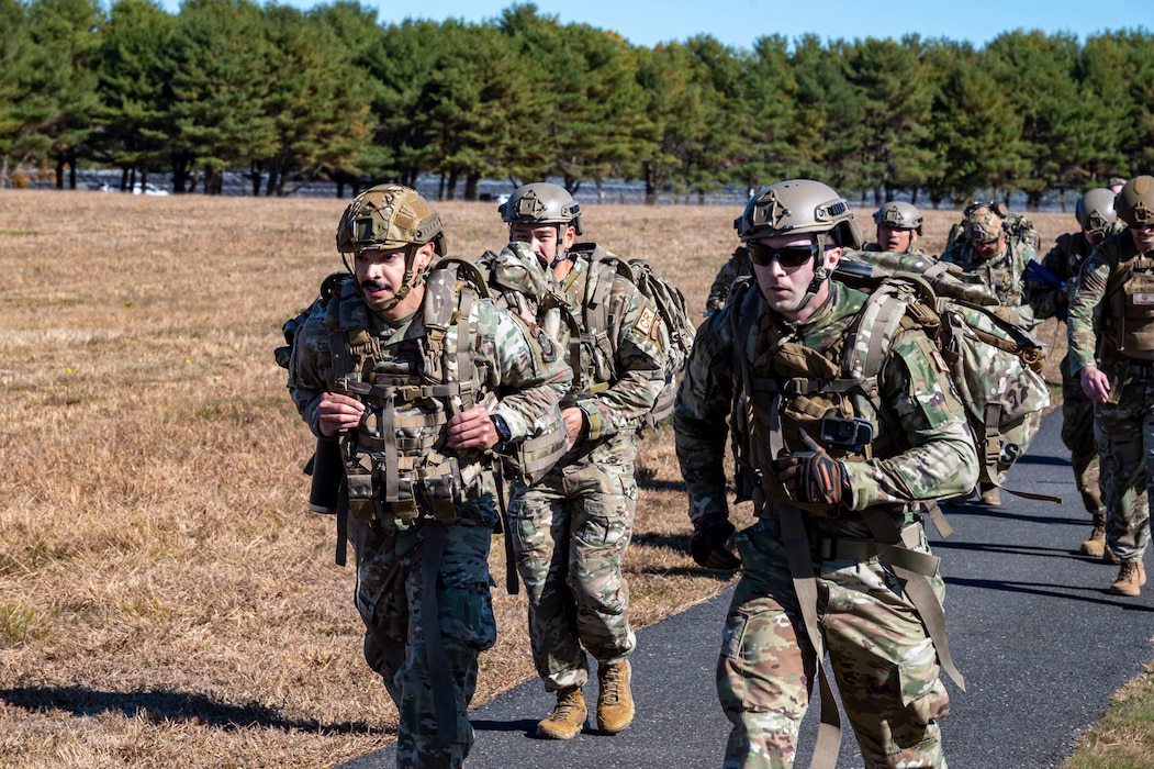Military members carry ruck sacks while marching outside.