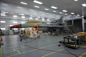 U.S. Air Force Airmen from the 20th Equipment Maintenance Squadron sand and paint an F-16 at Shaw Air Force Base, South Carolina, Oct. 20, 2021. The bumps on the body of the F-16 are sanded so the paint can be applied to a smoother surface. (U.S. Air Force photo by Senior Airman Dallin Wrye)