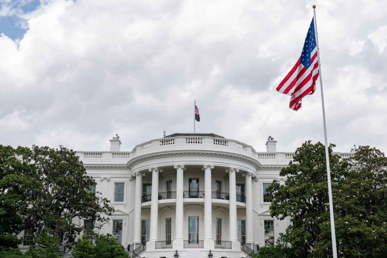 A view of a large white building during daytime, with a large American flag on a pole in front of it.