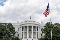 A view of a large white building during daytime, with a large American flag on a pole in front of it.