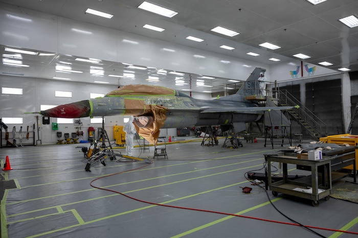 U.S. Air Force Airmen from the 20th Equipment Maintenance Squadron sand and paint an F-16 at Shaw Air Force Base, South Carolina, Oct. 20, 2021. The bumps on the body of the F-16 are sanded so the paint can be applied to a smoother surface. (U.S. Air Force photo by Senior Airman Dallin Wrye)