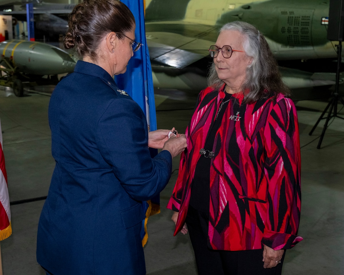 Dr. Heidi Ries, Air Force Institute of Technology provost and chief academic officer (right), receives her Air Force civilian Outstanding Career Service Award ribbon from retired U.S. Air Force commander, Air University Detachment 1 and AFIT director of staff, Col. Sarah Isbill (left), at her retirement ceremony at the United States National Museum of the Air Force, in Dayton, Ohio, on July 23, 2026.