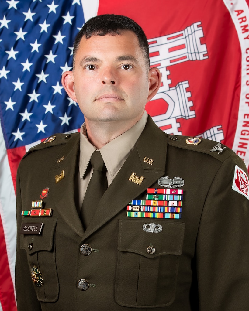Man in uniform wearing badges in front of the US and USACE flags.