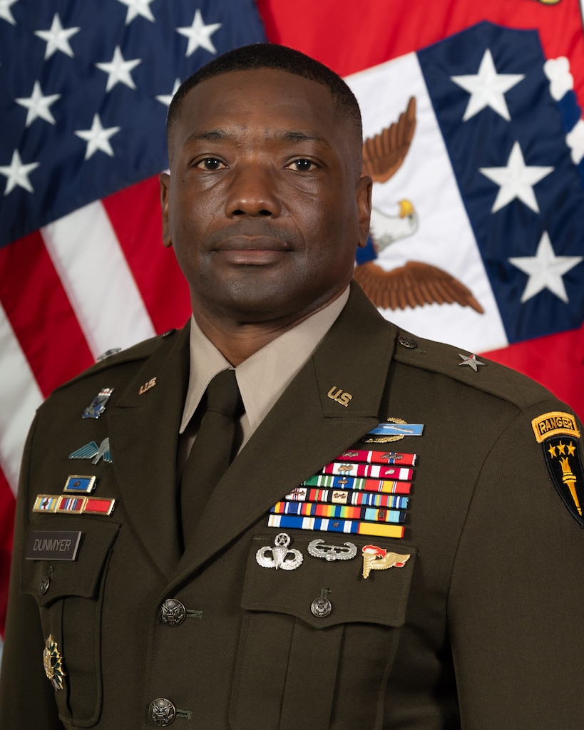 Headshot of BG Dunmyer, USAWC Commandant, smiling against a one star flag and American Flag.