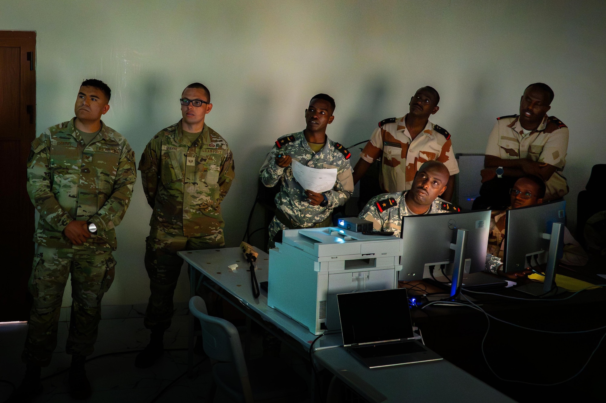 Military members all look to a screen in a classroom.