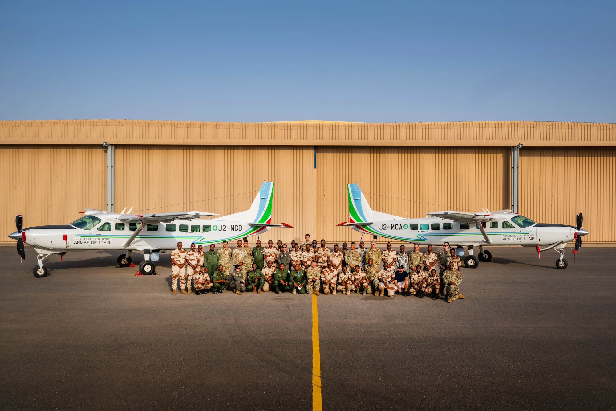 Military members stand together in a group between two aircraft for a group photo.