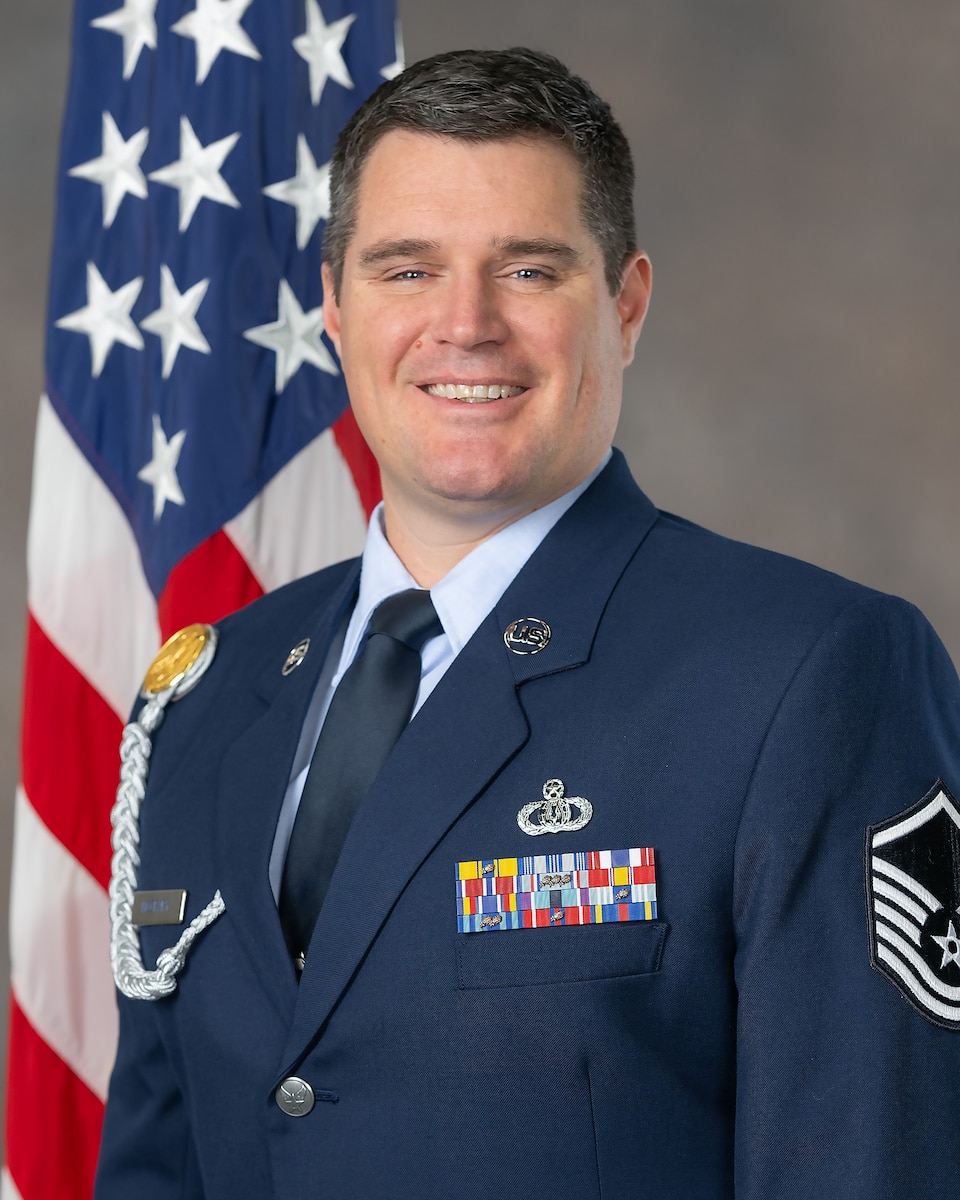 This photo depicts MSgt Will McCrary in service dress in front of an American Flag background