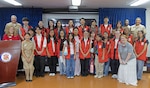 YOKOSUKA, Japan (July 31, 2026) – Capt. Joshua Miller, commanding officer of U.S. Navy Medicine Readiness and Training Command (USNMRTC) Yokosuka and director of U.S. Naval Hospital (USNH) Yokosuka, and American Red Cross staff pose for a group photo with the summer VolunTEEN participants at USNH Yokosuka. Twenty-six military-affiliated teens completed the six-week program, which provides hands-on professional development and gives participants insight into military healthcare by allowing them to shadow providers in 12 different hospital departments. (U.S. Navy photo by Ai Hazama, USNMRTC Yokosuka Public Affairs)