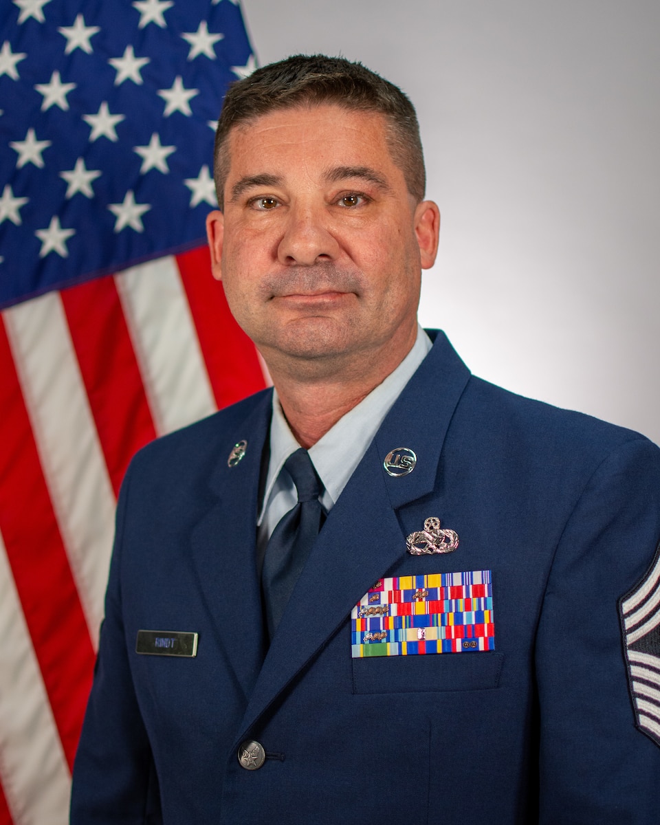 Service member poses for official portrait in front of US flag wearing their service dress blues