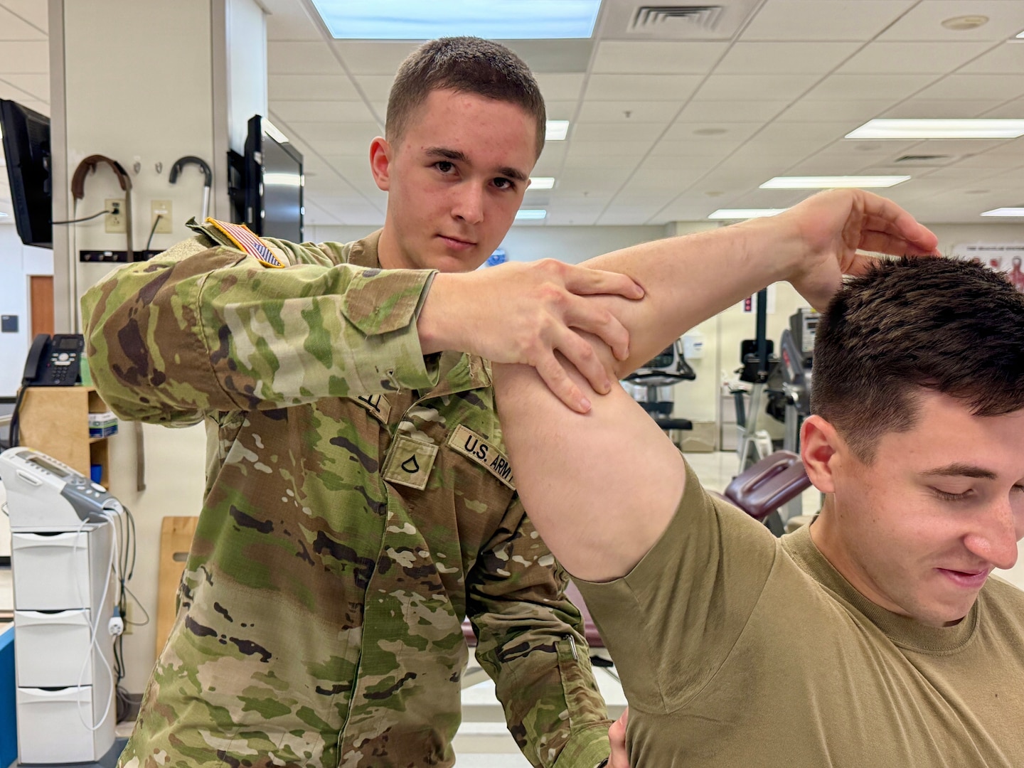 Soldier Therapist practices therapy on another Soldier's shoulder in a clinical setting.