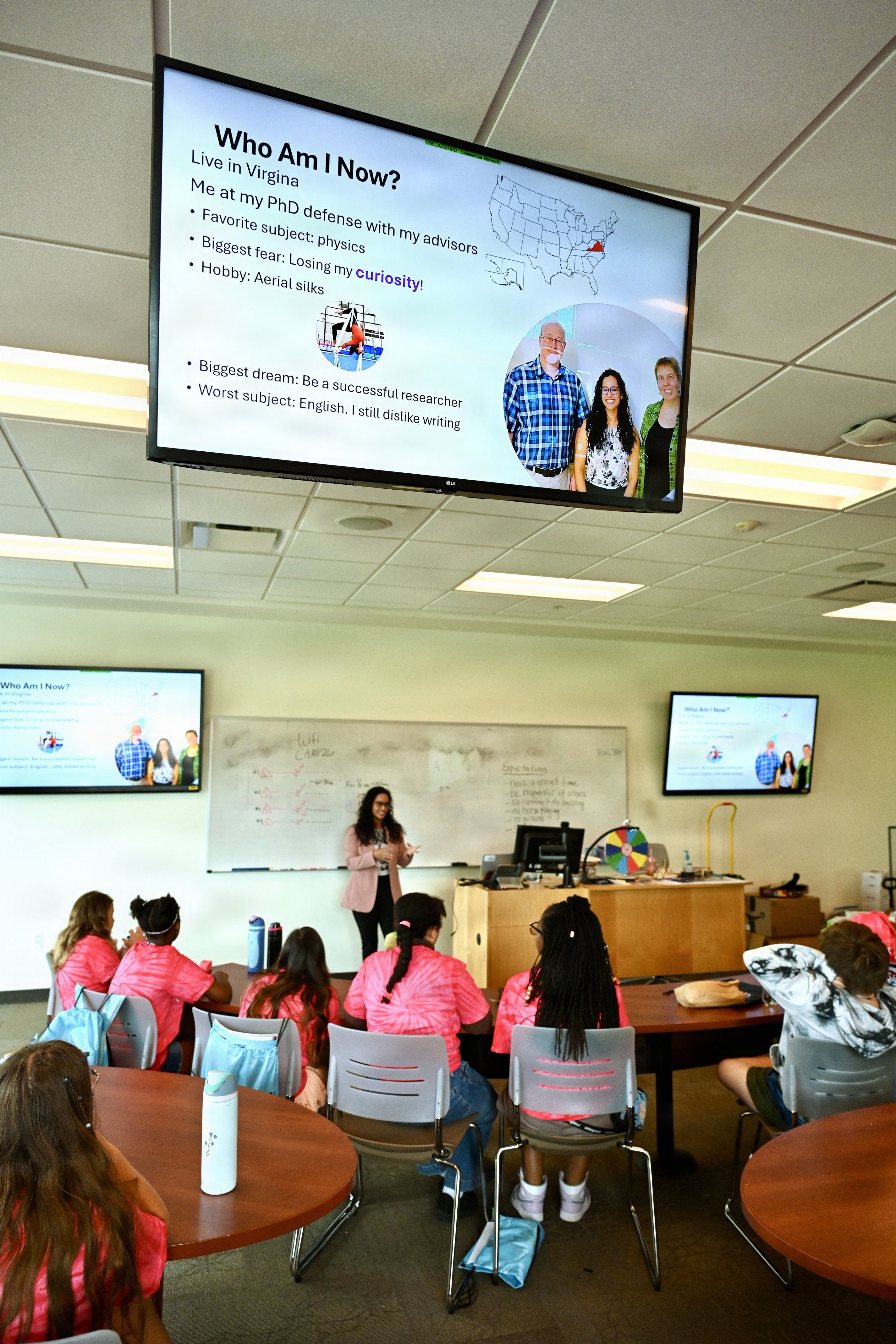 Guest speaker Charris Gabaldon, a NIWC Atlantic physicist embedded at NASA Langley, addresses middle school students at a podium during the STEM Rocks! summer camp.