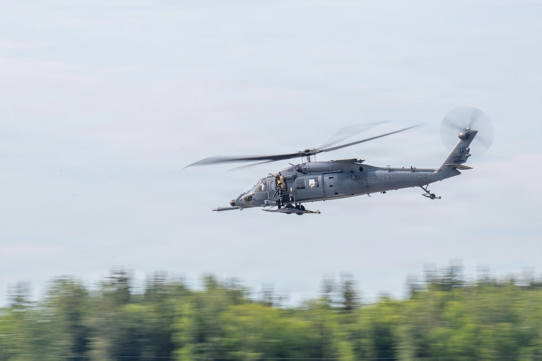 A helicopter flies in a blurry blue sky over a wooded area.