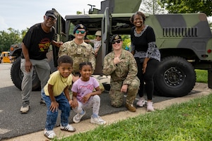 Service member talks to child in front of a military vehicle.