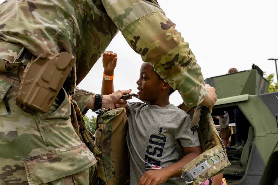 Service member talks to child in front of a military vehicle.