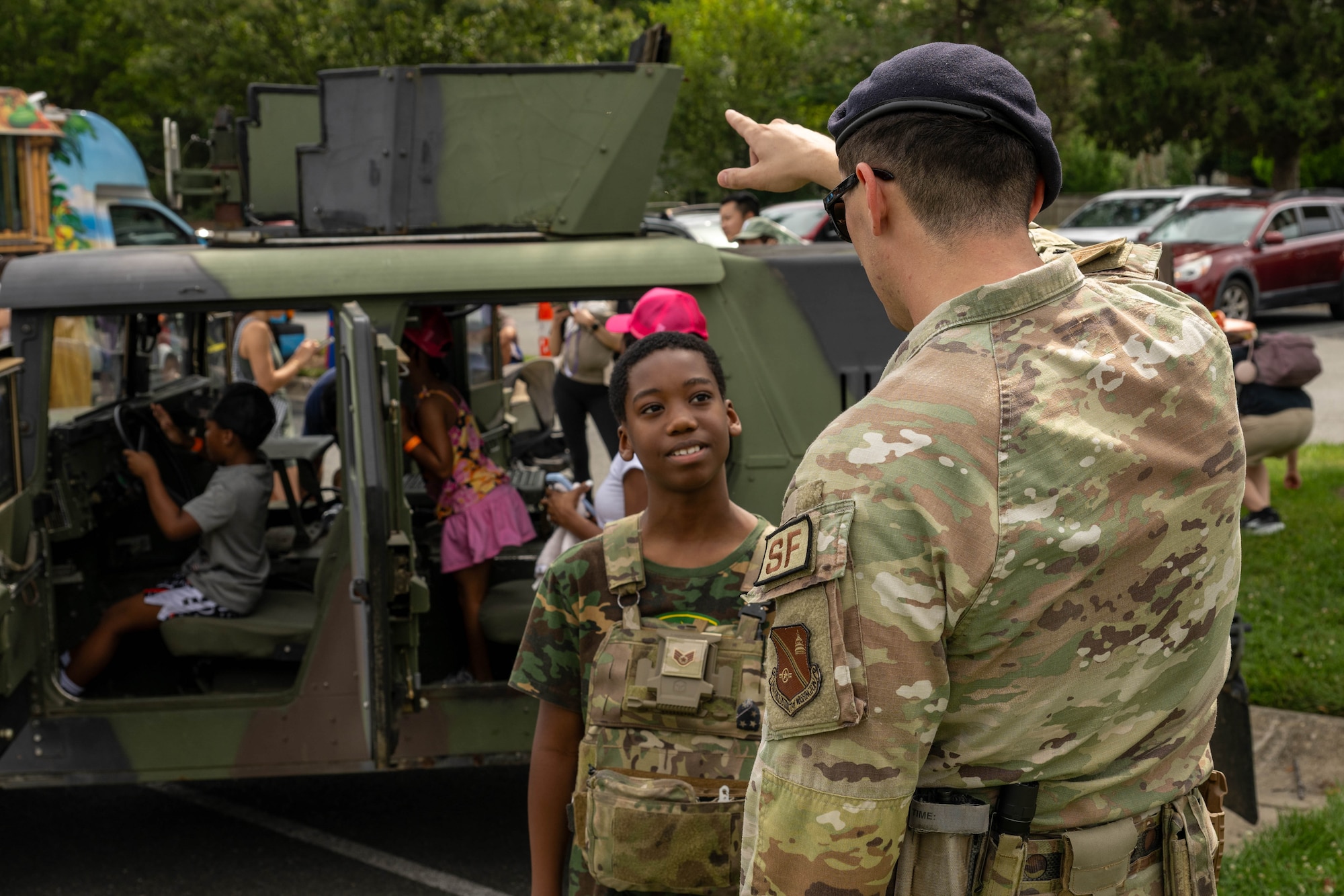 Service member talks to child in front of a military vehicle.