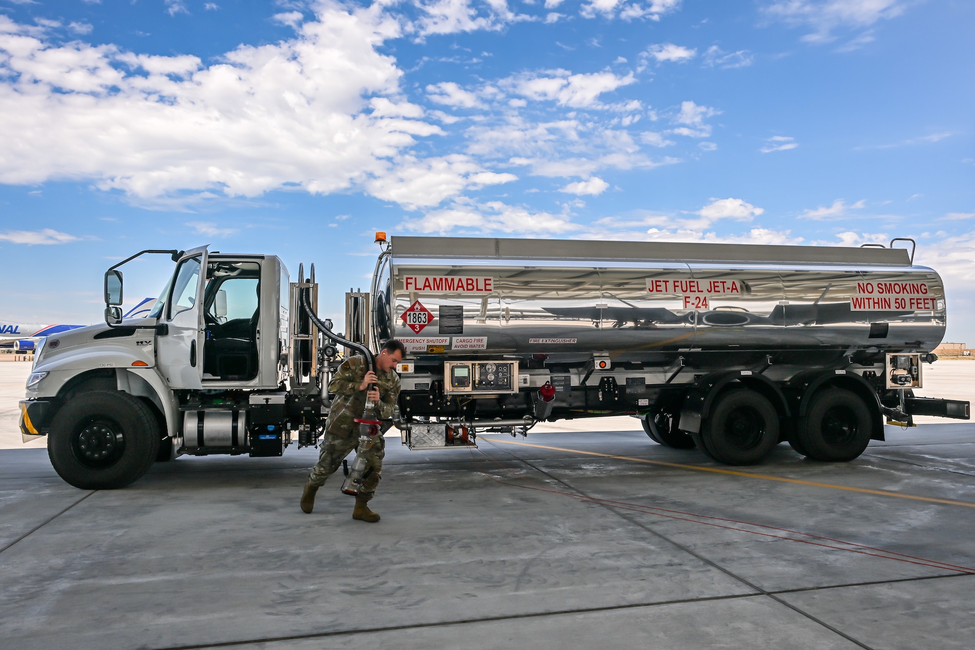 military airman pulling a fuel hose from a fuel tanker on airfield